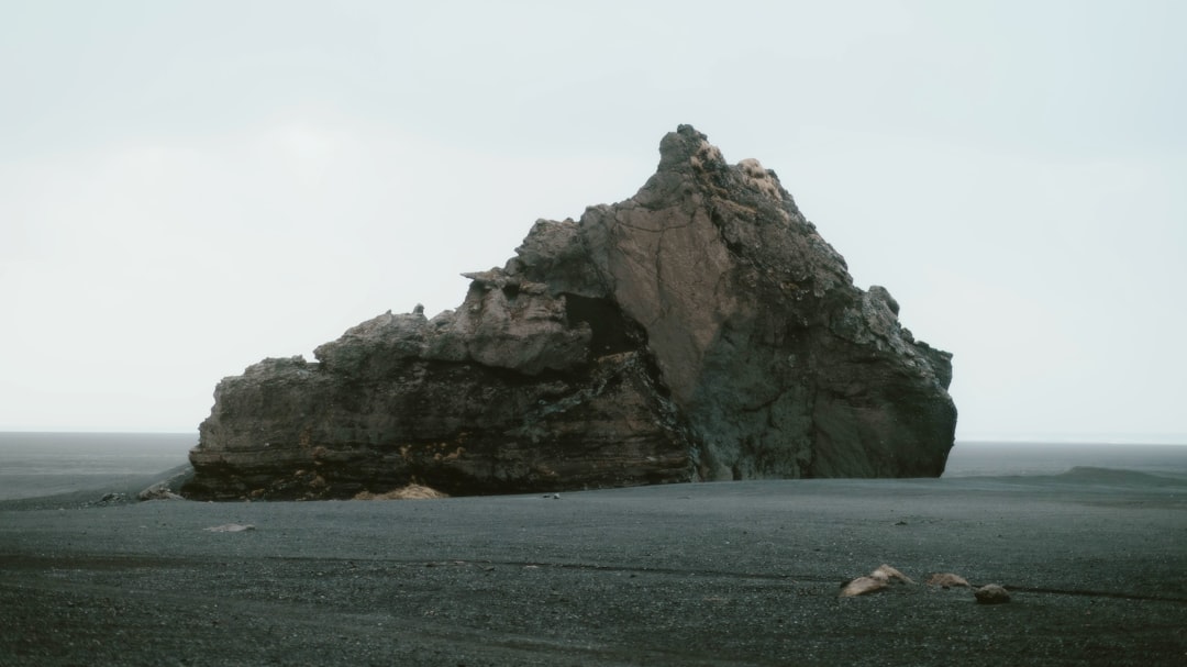 A large rock sits on a black sand beach.